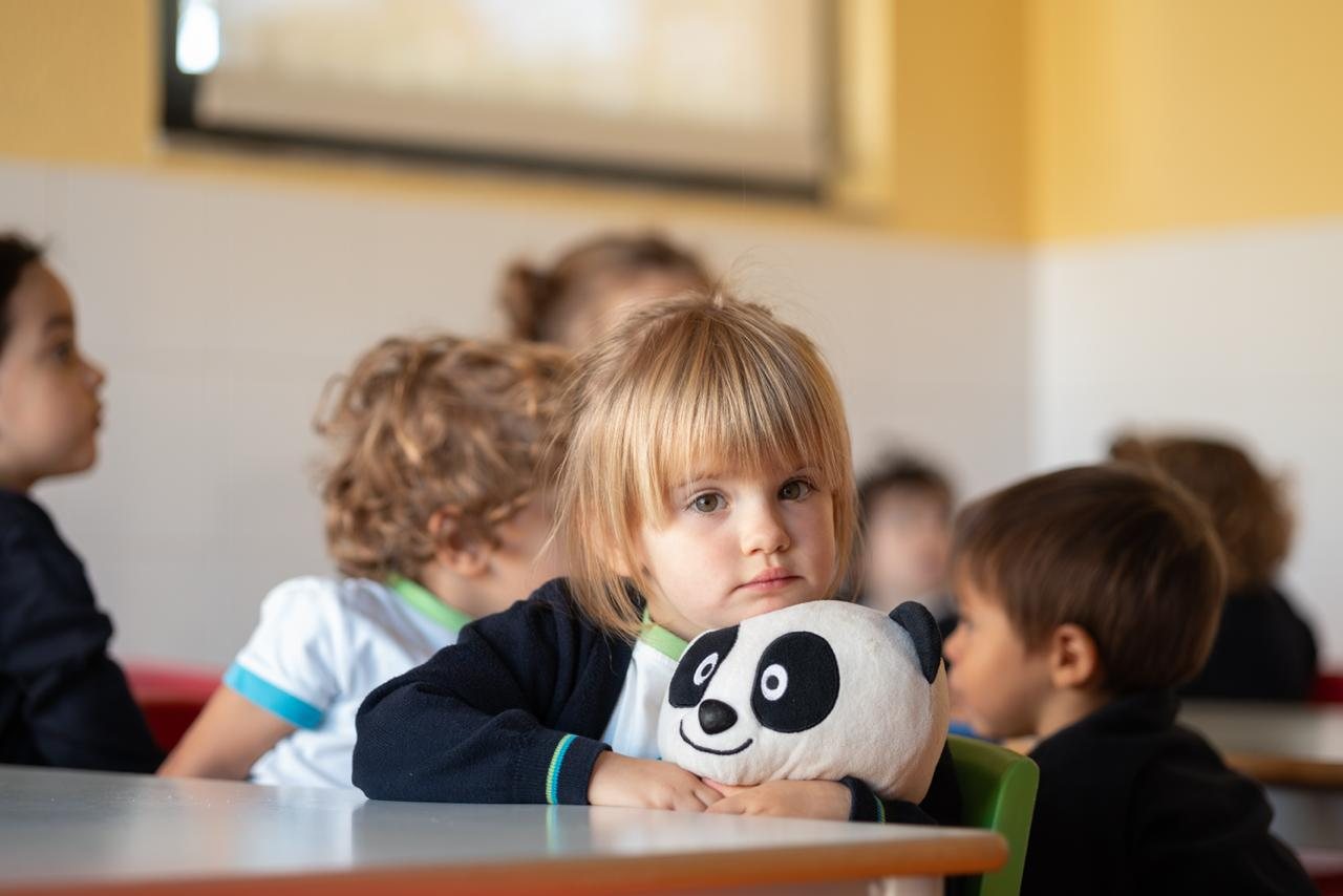 Um grupo de crianças sentadas à mesa, com um peluche de panda